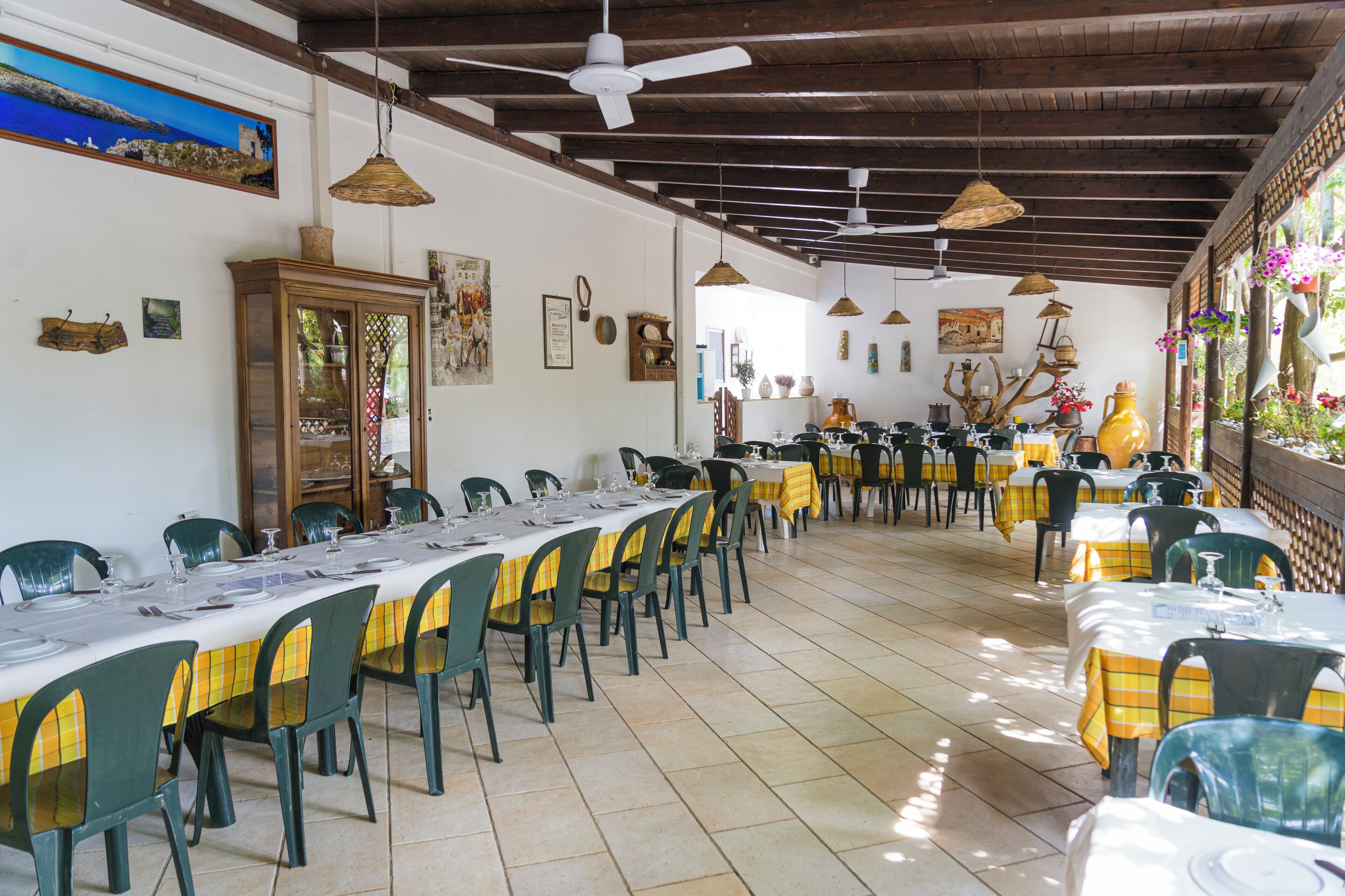 Een restaurant met meerdere tafels en stoelen, een plafondventilator en diverse wanddecoraties.