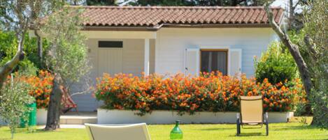 A white chair in a grassy area with a house in the background and a flower bed with orange flowers.