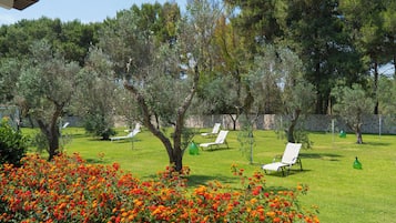 Un giardino con fiori arancioni, erba verde e poltrone da relax bianche.