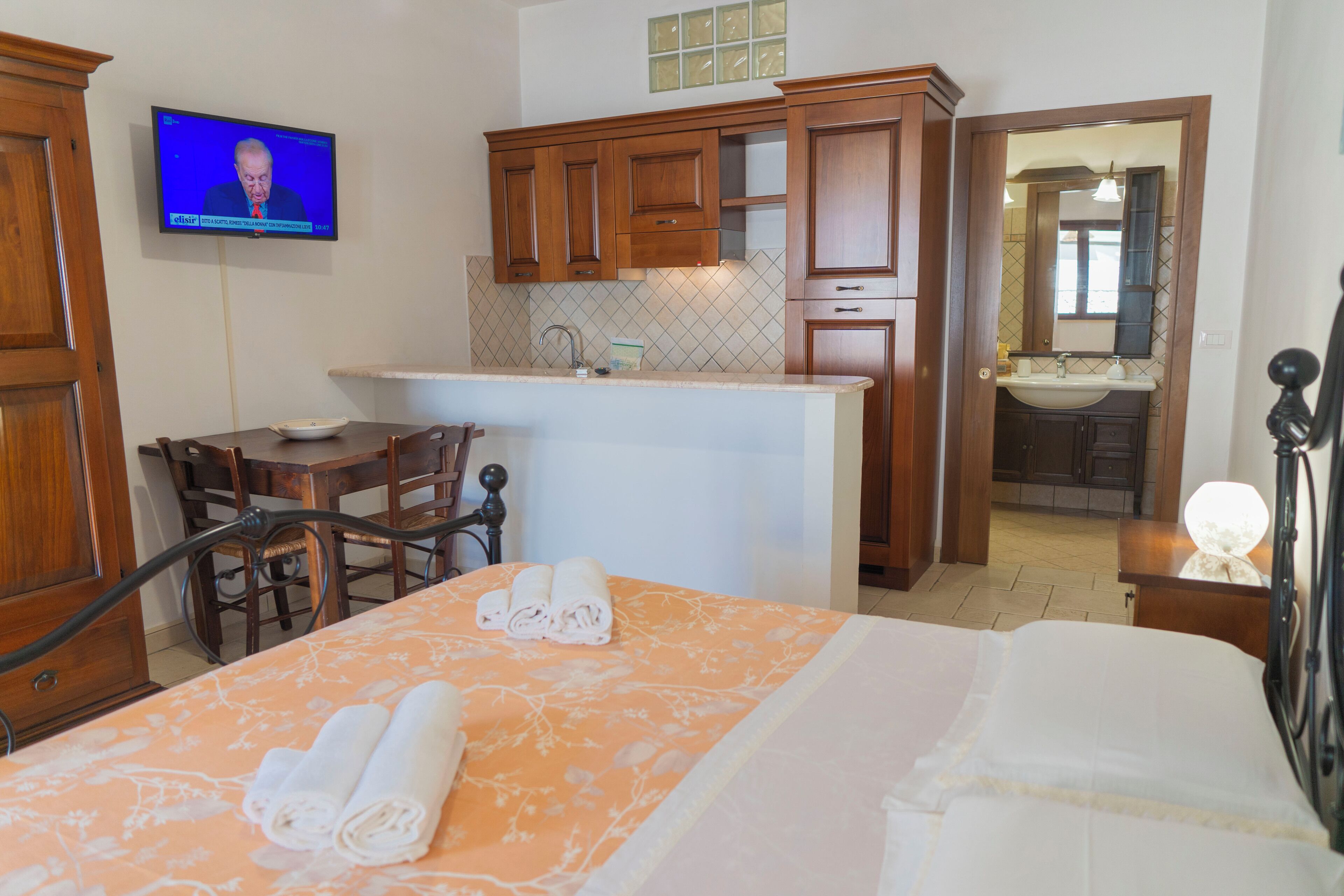 A hotel room with a bed, a desk, a television, a kitchen area, and a bathroom.