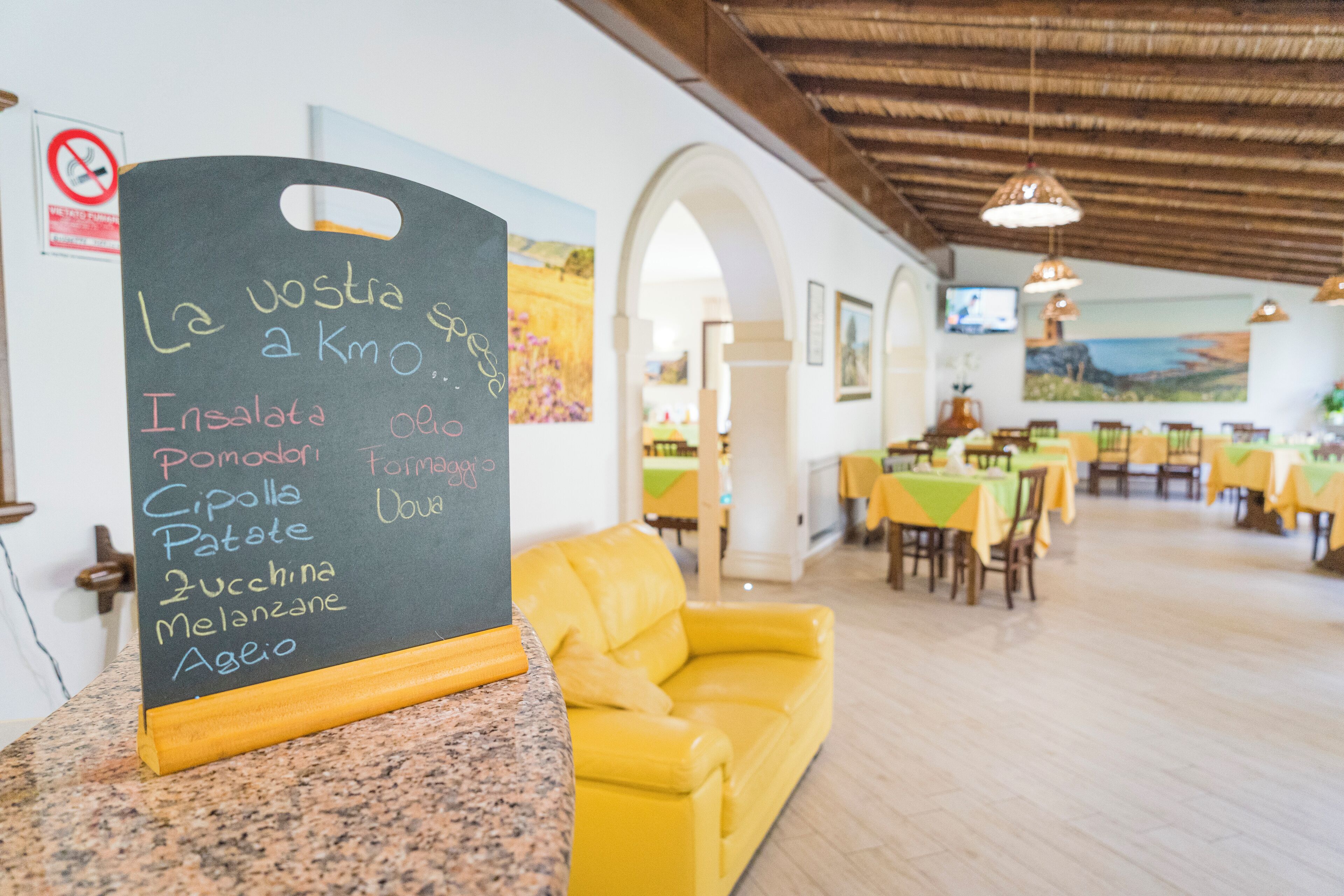 A restaurant with a chalkboard menu listing dishes like Insalata, Pomodori, Cipolla, Patate, Zucchina, Melanzane, and Ageo.