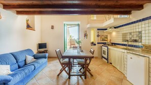 A cozy living area with a blue sofa, wooden dining table, and a kitchen with blue-tiled backsplash. - Corricella Hammok - Gioia Apartments (Procida)