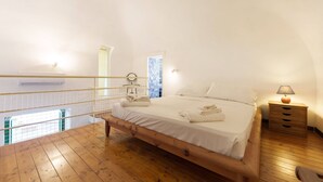 A bedroom with a wooden bed, a nightstand, a lamp, and a view of a pool through a window. - Corricella Hammok - Gioia Apartments (Procida)