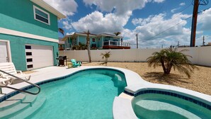 A swimming pool with a curved edge, a patio with chairs, and a house in the background. - Oceanview 3-bdrm home steps from beach!  Heated pool & hot tub.  Sleeps 6. (Fort Myers Beach)