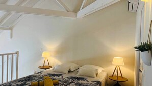 Quarto com cama, duas luminárias de cabeceira, ventilador de teto e um vaso com planta.