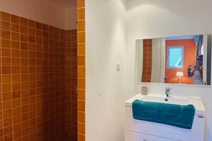 Un bagno con un lavandino bianco, uno specchio e una zona doccia con piastrelle arancioni.