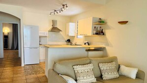 Uma sala de estar com sofá, área de cozinha com micro-ondas e mesa de jantar.