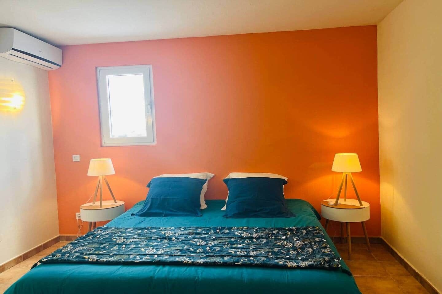 Una habitación con una cama, dos mesitas de noche con lámparas, una ventana y un equipo de aire acondicionado.
