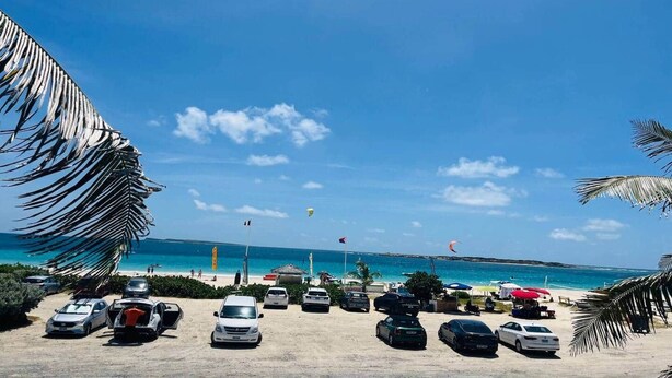 Uma praia com carros estacionados, céu claro e vista para o oceano.