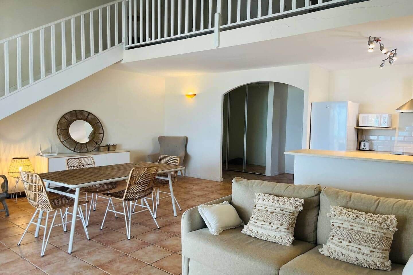 A spacious living area with a dining table, chairs, a sofa, a staircase, and a kitchen area.