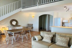 A spacious living area with a dining table, chairs, a sofa, a staircase, and a kitchen area.
