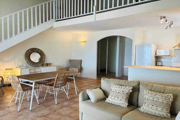 A spacious living area with a dining table, chairs, a sofa, a staircase, and a kitchen area.