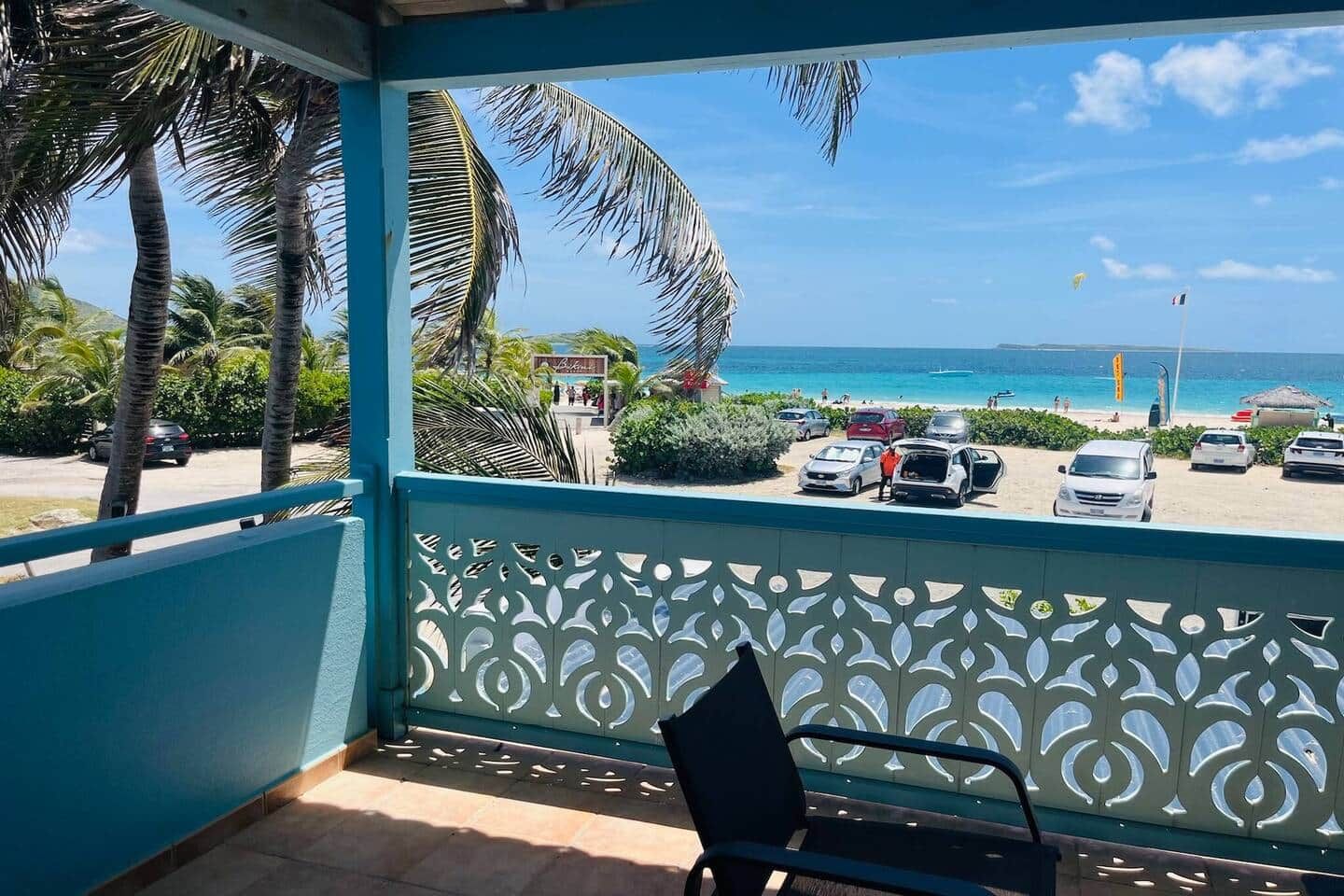 Un balcon avec vue sur une plage, des voitures garées et une enseigne indiquant « Baker's ».