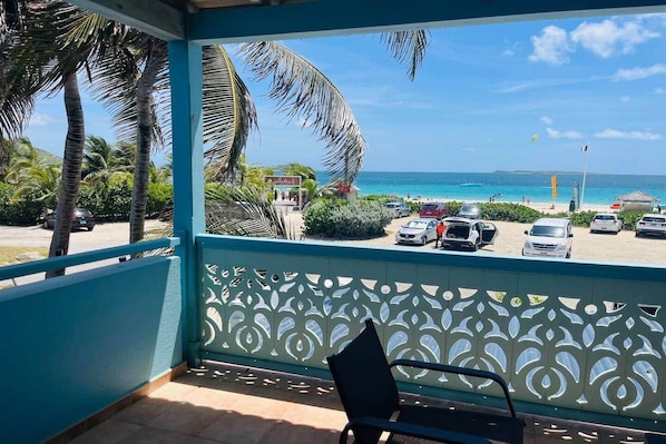 A balcony with a view of a beach, parked cars, and a sign for 'Baker's'.