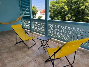 A balcony with yellow chairs, a small table, and a hammock.