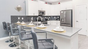 A modern kitchen with white cabinets, a central island with bar stools, a refrigerator, and a microwave. - Spacious villa with 10 bedrooms 4508 (Kissimmee)