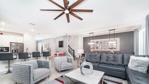 A modern living room with a grey sofa, two armchairs, a coffee table, and a dining area with a red table and chairs. - Spacious villa with 10 bedrooms 4508 (Kissimmee)