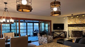A spacious living area with a large window, a stone fireplace, and a television. - Lakeside Hideaway- 3BR/4BA + Basement Gameroom in Connestee Falls Golf Community (Brevard)