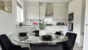 Una cocina moderna con armarios blancos, una isla central con cubierta de vidrio y sillas negras alrededor de una mesa de comedor de vidrio.