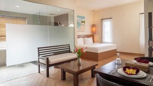 A hotel room with a bed, a bench, a dining table with a vase of flowers, and a painting on the wall. - Swiss-Belcourt Sunset (Bali)
