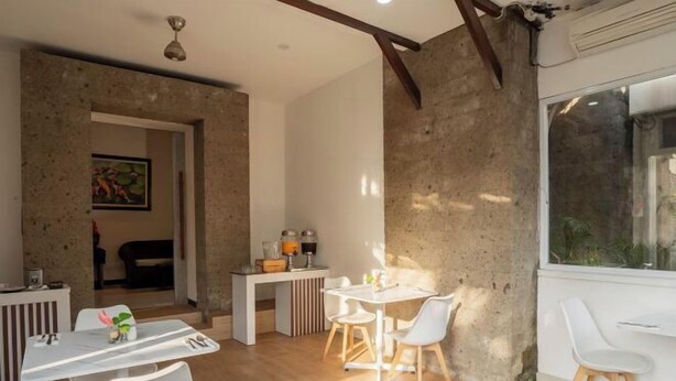 A modern dining area with a white table and chairs, a kitchen counter with appliances, and a large window providing natural light. - Swiss-Belcourt Sunset (Bali)