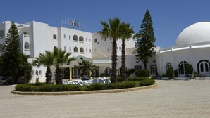 A white building with arched windows and a dome, surrounded by palm trees and a paved courtyard. - Miramar Sharm ElKantaoui (Port El Kantaoui)