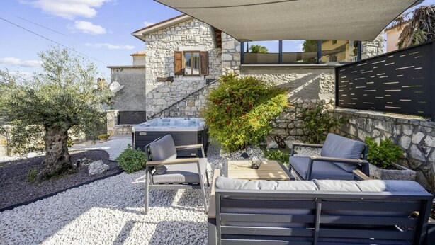 Un patio moderno al aire libre con muros de piedra, un jacuzzi y mobiliario exterior.