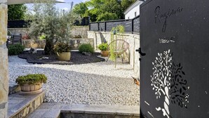 Un jardín con un sendero de grava, plantas en macetas y un muro de piedra.