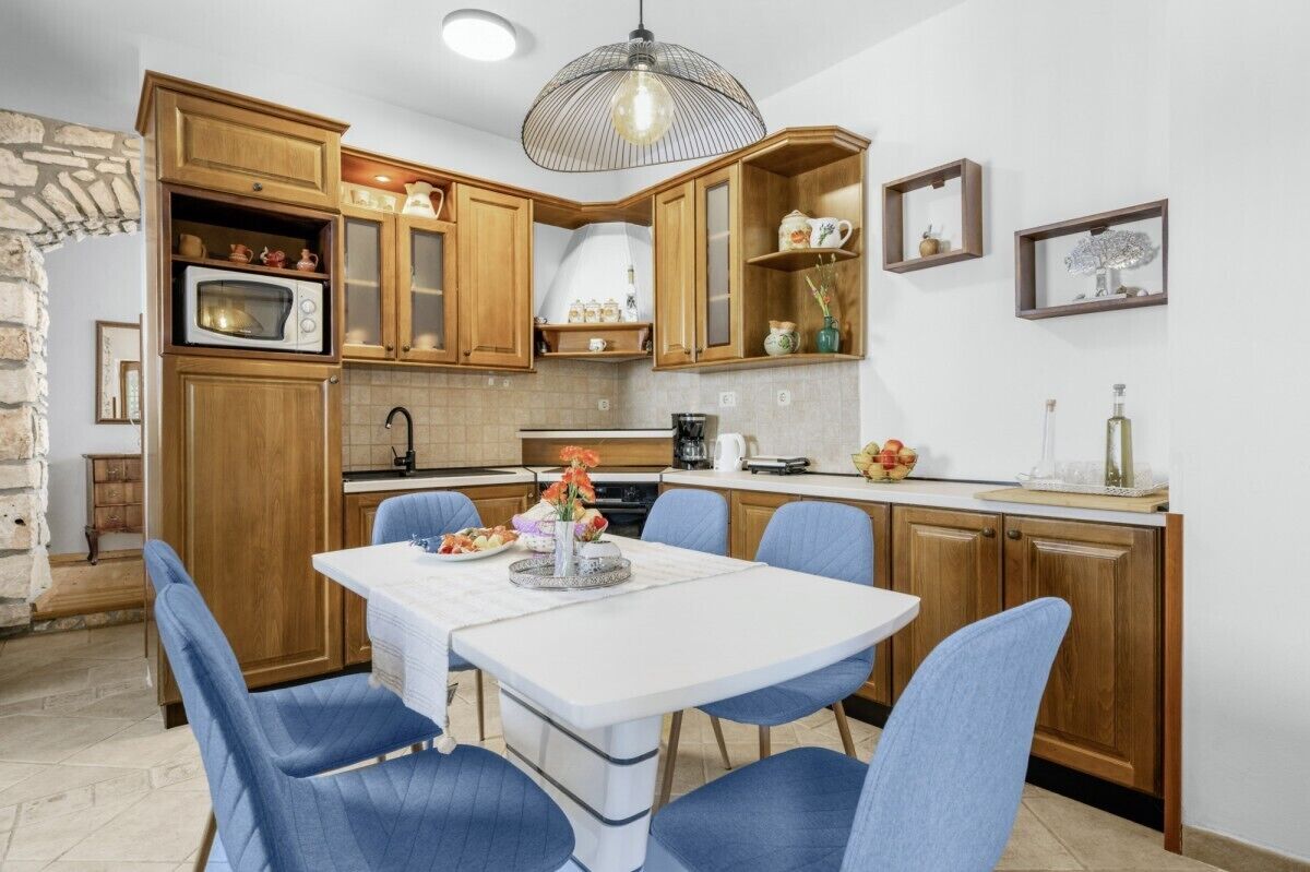 Une cuisine avec des meubles de rangement en bois, une table à manger blanche et des chaises bleues.