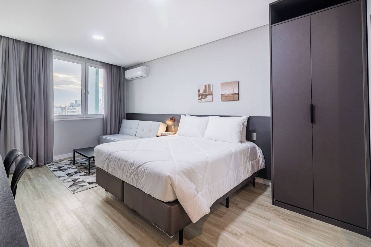 A modern hotel room with a large bed, a desk, and a wardrobe.