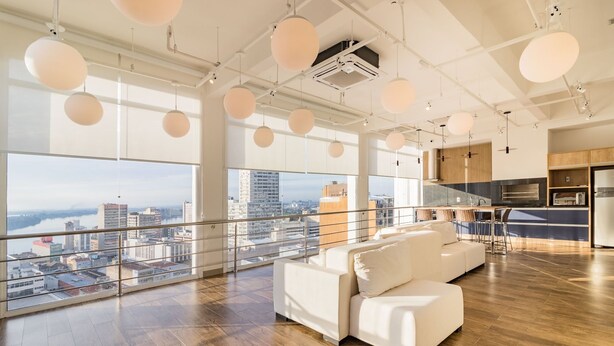 A spacious living area with a large window overlooking a cityscape, a modern kitchen, and a balcony with a railing. - Town.Co Housi by My Way (Porto Alegre)