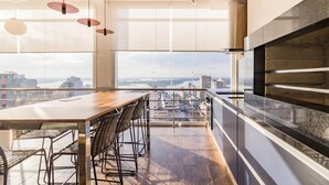 A modern kitchen with a large island, a dining area with chairs, and a view of the city through large windows. - Town.Co Housi by My Way (Porto Alegre)
