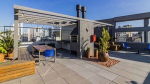 A rooftop terrace with a wooden table and chairs, potted plants, and a view of the cityscape. - Town.Co Housi by My Way (Porto Alegre)