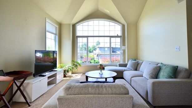 A living room with a large window, a television, a sofa, and a coffee table. - Wonderful 4-bdrm, 2.5 bath home in Renton,15 min to Seattle,2 min to Coulon Park (Renton)