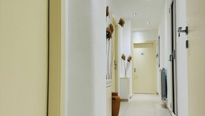 A clean, well-lit hallway with cream-colored walls and white tiled flooring. There are doors on the left and right, a potted plant with dried flowers on the right, and a radiator on the right wall. - Charming apartment with 3 bedrooms and WiFi, AC in marvelous Catania (Catania)