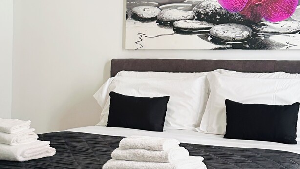 A hotel room with a bed, pillows, and a wall-mounted picture of rocks and a flower. - Charming apartment with 3 bedrooms and WiFi, AC in marvelous Catania (Catania)