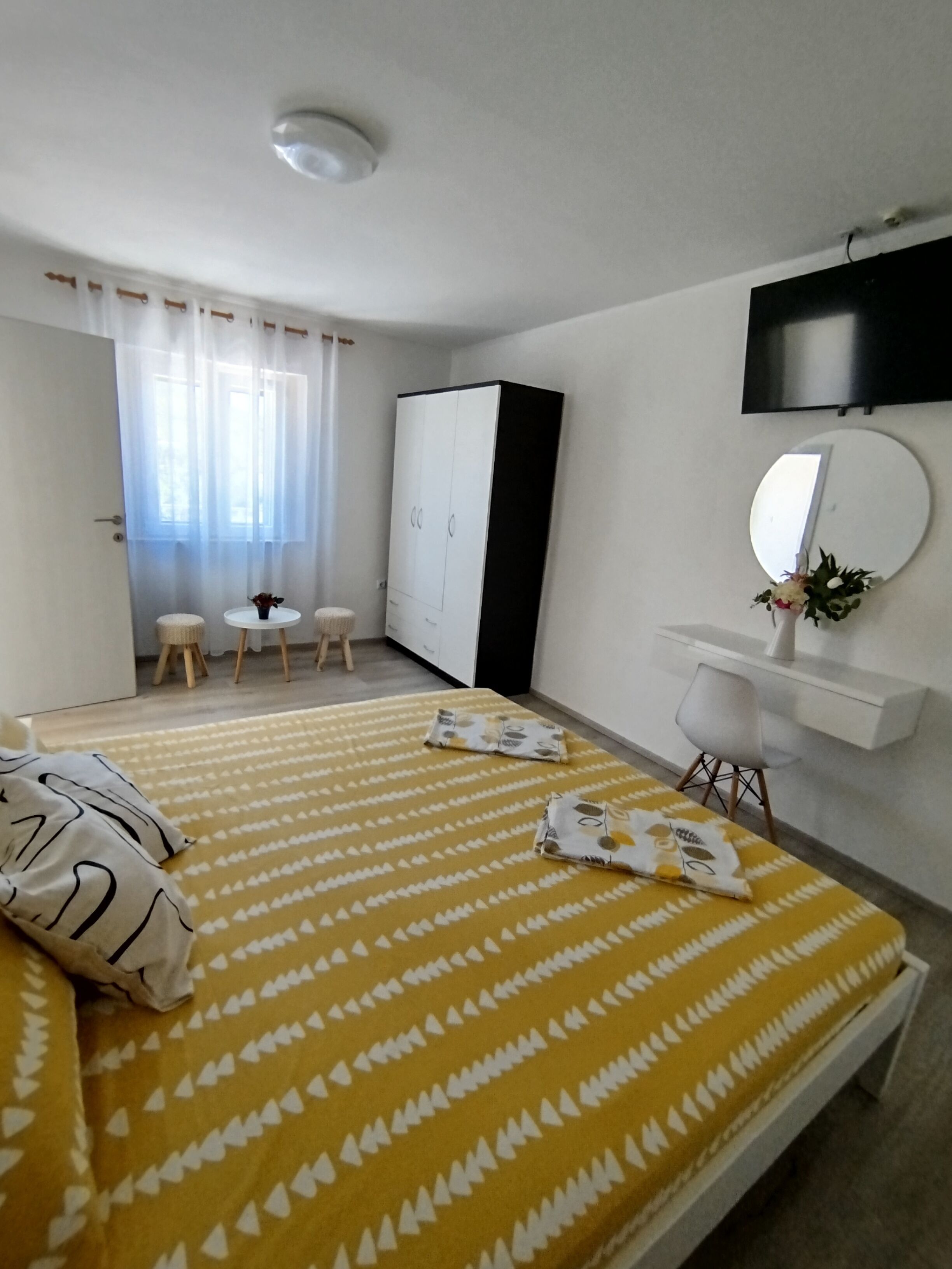 A hotel room with a bed, a wardrobe, a desk with a mirror, and a television on the wall.