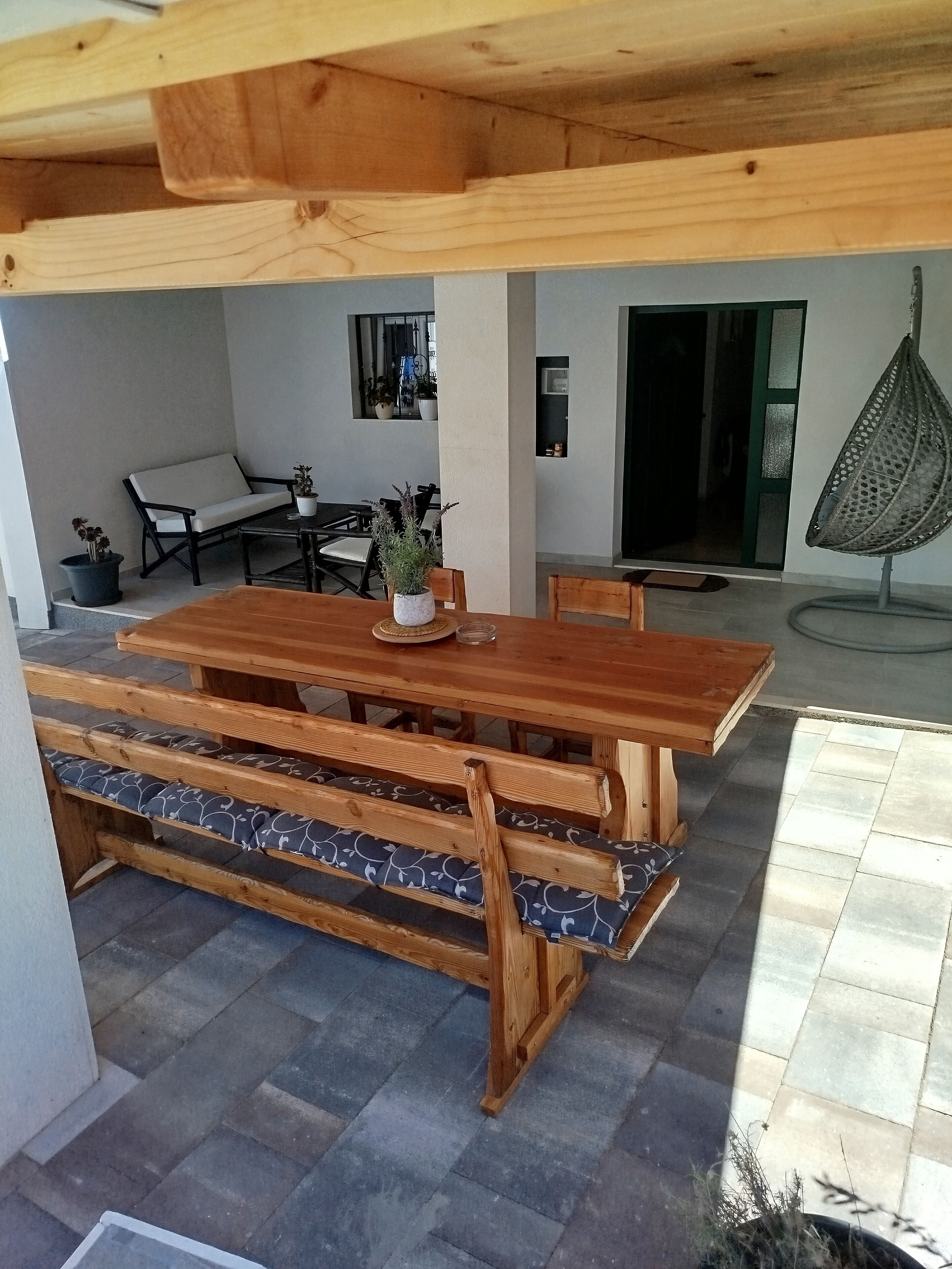 Una mesa de comedor de madera con bancos, una silla colgante y plantas en macetas.