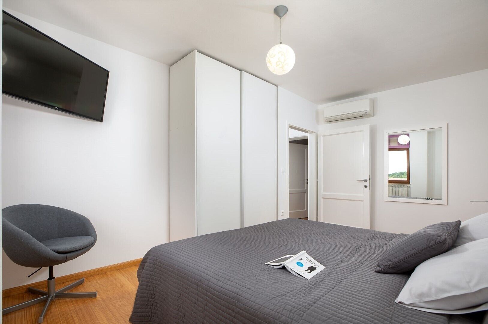 Een slaapkamer met een bed, een stoel, een kledingkast, een televisie en een spiegel.