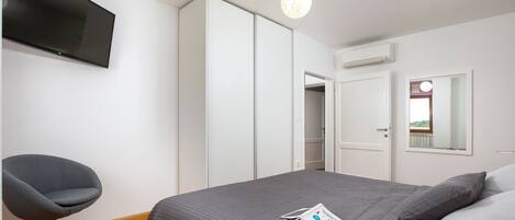 Een slaapkamer met een bed, een stoel, een kledingkast, een televisie en een spiegel.