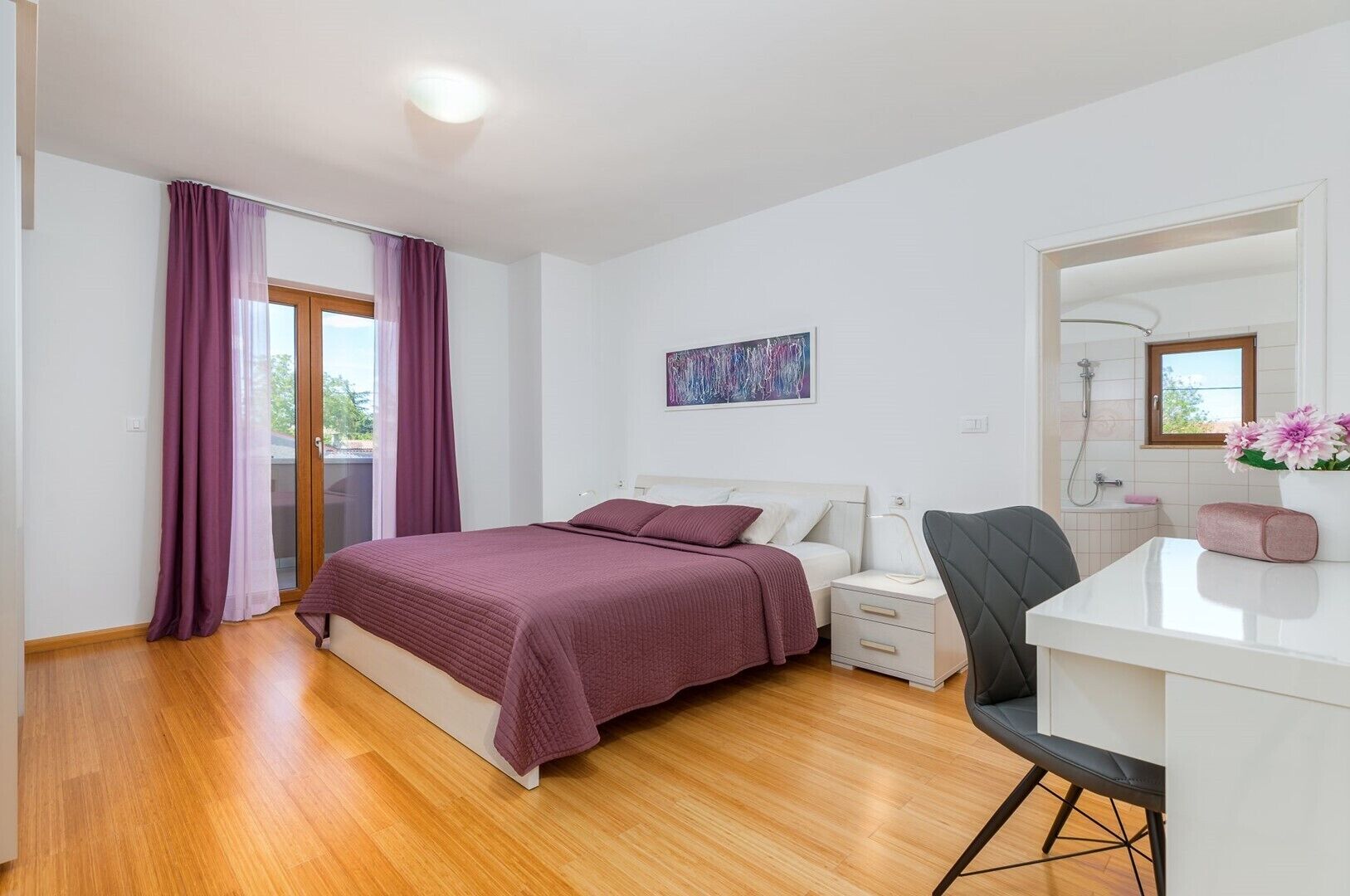 Ein Schlafzimmer mit Bett, Nachttisch, Stuhl und einem durchgegangenen Tür sichtbaren Badezimmer.