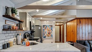 A modern kitchen with a marble countertop, wooden cabinets, and a wooden dining area. - 3BR Cozy Cottage, AC, BBQ, Fast Wi-Fi, Fireplace, Firepit, Walk to Beach (Pocono Lake)