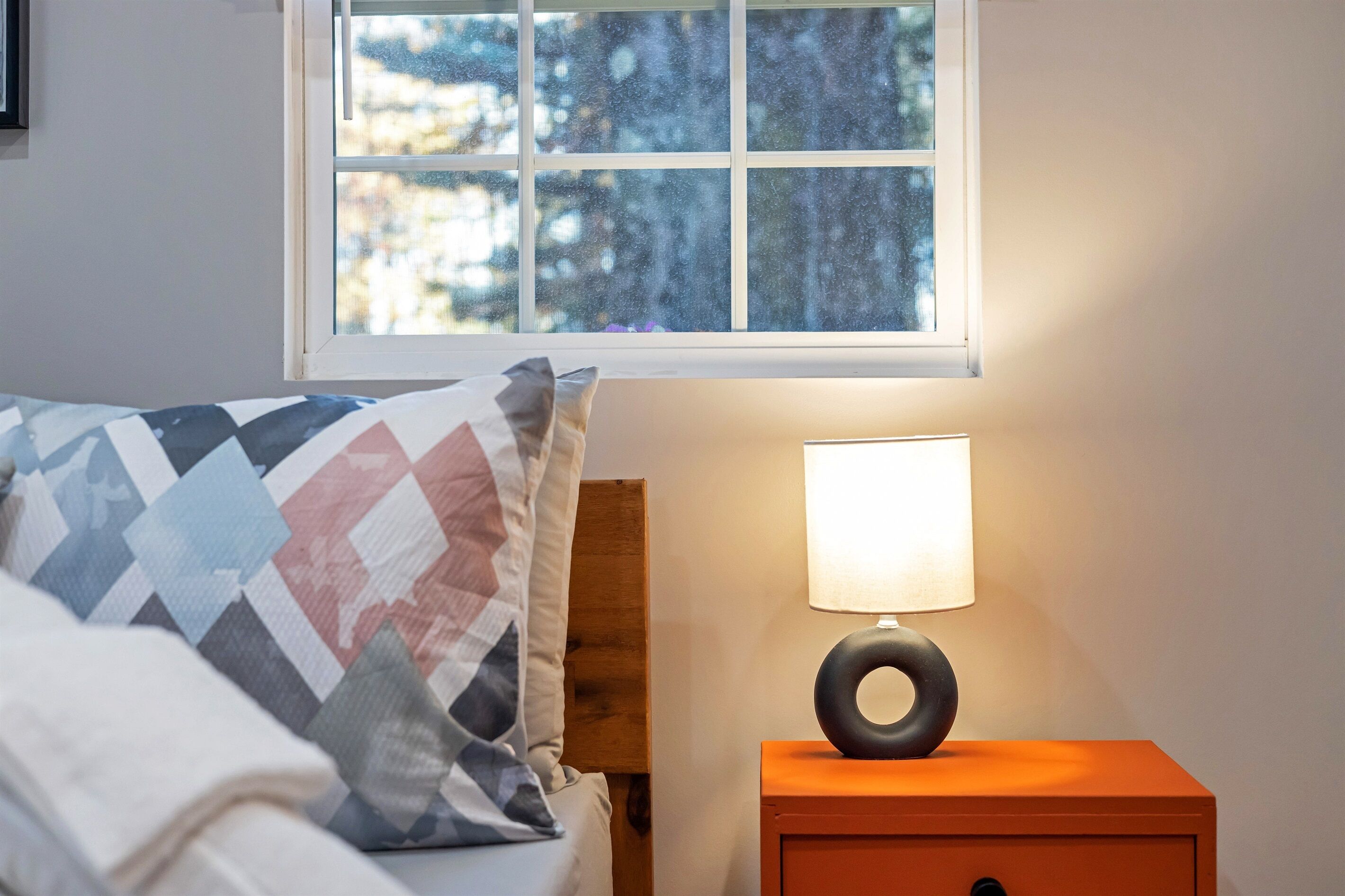 Una camera da letto con un letto, un comodino con una lampada e una finestra vista alberi.