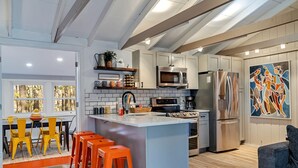 A modern kitchen with white cabinets, stainless steel appliances, and a central island with bar stools. - 3BR Cozy Cottage, AC, BBQ, Fast Wi-Fi, Fireplace, Firepit, Walk to Beach (Pocono Lake)