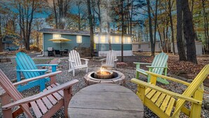 A cozy outdoor seating area with Adirondack chairs and a central fire pit. - 3BR Cozy Cottage, AC, BBQ, Fast Wi-Fi, Fireplace, Firepit, Walk to Beach (Pocono Lake)