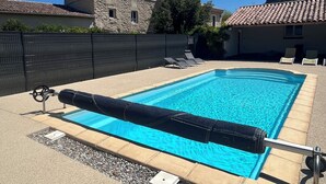 A rectangular swimming pool with a clear blue water, surrounded by a concrete deck. There are lounge chairs along the poolside.