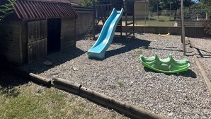 A playground with a blue slide, a wooden climbing structure, and a green boat-shaped swing.