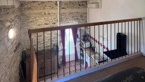 A room with a stone wall, a wooden railing, and a view of a staircase leading to another level.