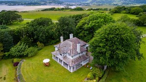 A large, two-story house with a spacious front lawn and a view of a river and mountains in the distance.