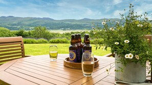 Una mesa de madera con tres botellas de cerveza, un vaso de cerveza y una planta en maceta con flores blancas.